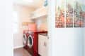 Laundry room with red washer and dryer, white cabinets, abstract wall art, and a patterned laundry basket.