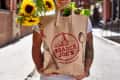 Person holding Trader Joe's paper bag with sunflowers and lettuce.
