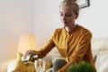 Woman in mustard blouse pouring white wine into a glass on a beige sofa.
