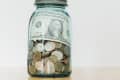 Jar filled with coins and a one-dollar bill on a wooden surface.