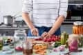 Person slicing radishes on a kitchen counter surrounded by jars of pickled vegetables and fresh ingredients.