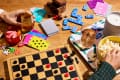 Board game setup with checkers, playing cards, dominoes, popcorn, and drinks on a wooden table.
