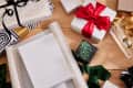 Gift wrapping scene with various wrapped presents, ribbons, and wrapping paper on a wooden surface.