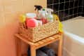 A basket full of cleaning supplies next to the tub in an orange and black tiled bathroom