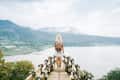 Person with a backpack standing on a wooden platform overlooking a lake and mountains.