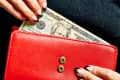 Hands holding a red wallet with a twenty-dollar bill partially visible.