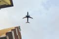 Airplane flying overhead with building corners visible in the foreground.