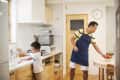Man in apron setting table with fruit while child washes hands in kitchen.