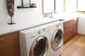Laundry room with front-loading washer and dryer, wooden cabinets, wall art, and a decorative mask.