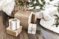 Gift boxes wrapped in brown and white paper with twine bows under a decorated Christmas tree.