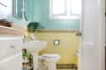 Small bathroom with yellow tiled walls, pedestal sink, and green plant decor under a window.