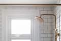 Bathroom with white subway tiles, brass showerhead, window, and corner shelf with bottles.