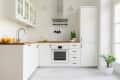 Modern white kitchen with wooden countertops, potted plant, oranges, and a stainless steel oven.