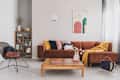 Flowers in vase on wooden coffee table in fashionable living room interior with brown corner sofa with pillows and abstract painting on the wall