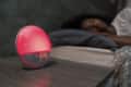 Modern digital alarm clock counting down time to awakening on bedside table near sleeping black female in morning at home