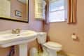Small cozy peach color bathroom with white toilet and washbasin.