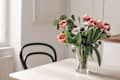 Spring flowers in glass vase on wooden table. Blurred kitchen background with old chair. Bouquet of red tulips, white anemone flowers and eucalyptus branches. Contemporary elegant scandi interior.