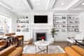 ELMHURST, IL, USA - MARCH 30, 2021: A luxurious, white living room with a coffered ceiling, a television mounted above a tiled fireplace, and built in shelving in front of chairs and a couch.