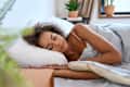 Young calm African American woman model sleeping well on her side with eyes closed lying in comfortable bed on orthopedic mattress lying on soft pillow at home having healthy night sleep relaxing in the morning.