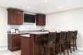 ELMHURST, IL, USA - NOVEMBER 1, 2020: A basement wet bar with dark wood cabinets, bar stools sitting at the island, a mounted television, and granite countertops.