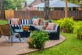 Outdoor furniture - striped sectional on round patio with area rug and chair and ferns with trees and neighboring houses in background