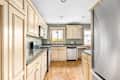 An apartment kitchen with light wood cabinets, stainless steel appliances, and green walls.