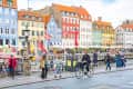 Cyclist, pedestrians and tourists in Christianshavn, Nyhavn neighborhood, Copenhagen, Denmark with traditional Danish colorful houses, boats and flags on background