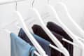 Many blue denim jeans hanging on white clothes hangers on clothing rack. Close up of folded casual denim jeans in wardrobe with coat hangers
