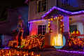 Illuminated Halloween house outdoor decorations with orange and purple garlands, skeleton, pumpkins and ghosts near the house porch