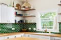 A kitchen detail with butcher block wood countertops, white cabinets, a gold fixture hanging over the island, and green subway tile backsplash.