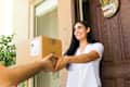 Smiling young woman is receiving a package from a delivery man at the entrance of her home