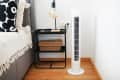 White tower fan next to a bed and bedside table with a lamp in a modern bright interior