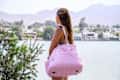 Stylish woman looks out over a tranquil lake, sporting a chic pink duffel bag
