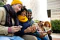 Young multiracial college student friends looking at mobile phones during winter day. Technology and lifestyle.