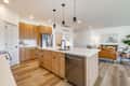 Modern kitchen and dining room interior staged for real estate with kitchen island bar stools stainless appliances hardwood floor sink pendant lighting bright sunny mixed wood cabinets table setting
