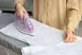 Young woman ironing white clothes on board at home, closeup