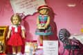 Two dolls in vintage outfits on display, one in a red polka dot dress, the other in a blue floral dress with a hat.