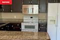 Kitchen with dark wood cabinets, granite countertops, white appliances, and a large island.
