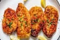 Crispy breaded fish fillets garnished with parsley and lemon wedges on a white plate.
