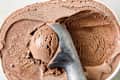 Chocolate ice cream in a white container with a metal scoop, showing a smooth, creamy texture.