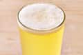 A glass of pale beer with a frothy head next to a yellow can labeled "Allagash White."