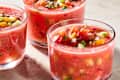 Chilled gazpacho in clear bowls topped with diced vegetables, accompanied by toasted bread slices.