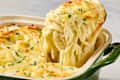 Creamy baked pasta with melted cheese and parsley, being served from a green dish.