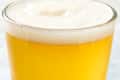 A close-up of a glass filled with golden beer topped with a thick, frothy head and bubbles.