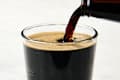 A dark beverage being poured into a clear glass, creating a frothy head.