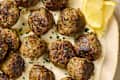 Savory meatballs garnished with parsley, served on a creamy sauce with lemon wedges.