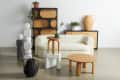Modern living room with a cream sofa, wooden tables, geometric sculptures, and plants on a wooden cabinet.