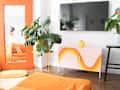 Living room with orange sofa, large mirror, pink cabinet with orange wave design, and potted plants.
