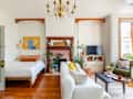 Living room with a white sofa, green armchair, TV, plants, and a bed. Chandelier and colorful artwork above the bed.