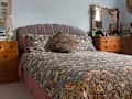 A bed with floral sheets and wooden bedroom furniture.